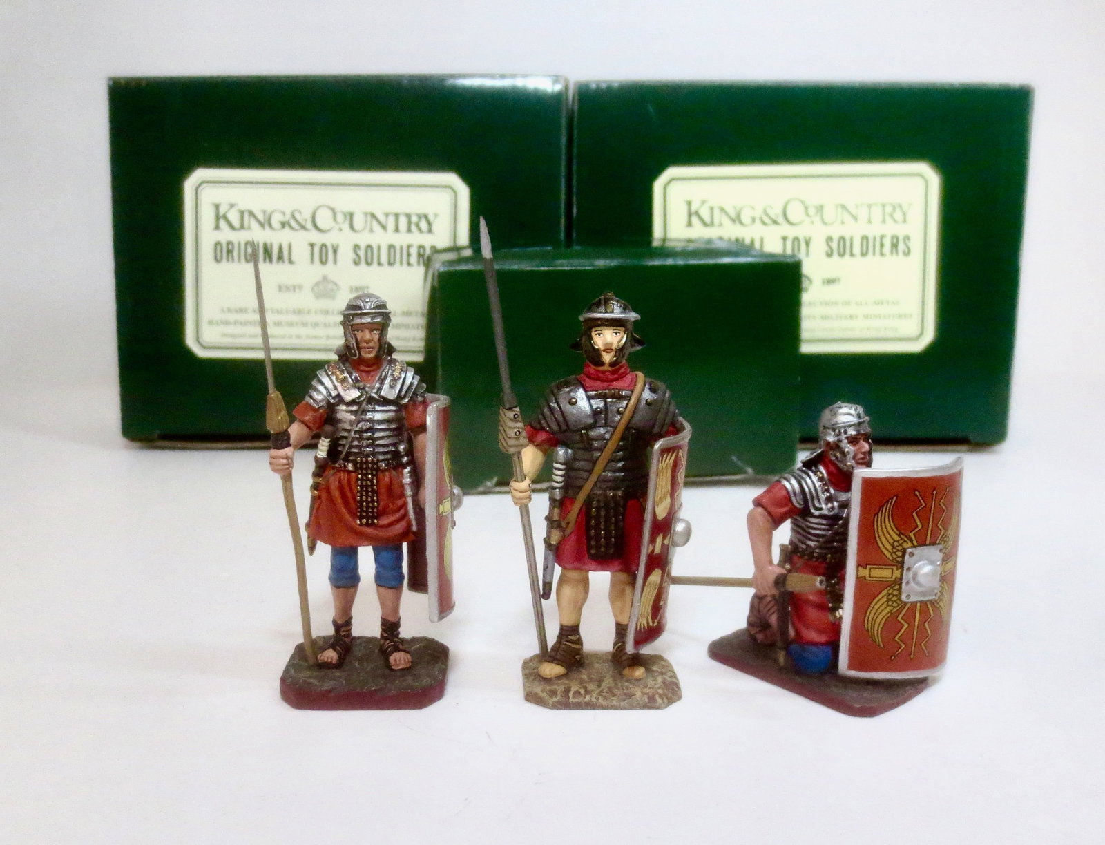 King & Country Romans: #R023-RE Legionary Standing with Spear, #R028-RE Kneeling with Spear, and Scarce K&C Classics Legionary Standing At Ease #R006. 3 pieces. Kneeling figure missing spear tip, others in Mint condition. B