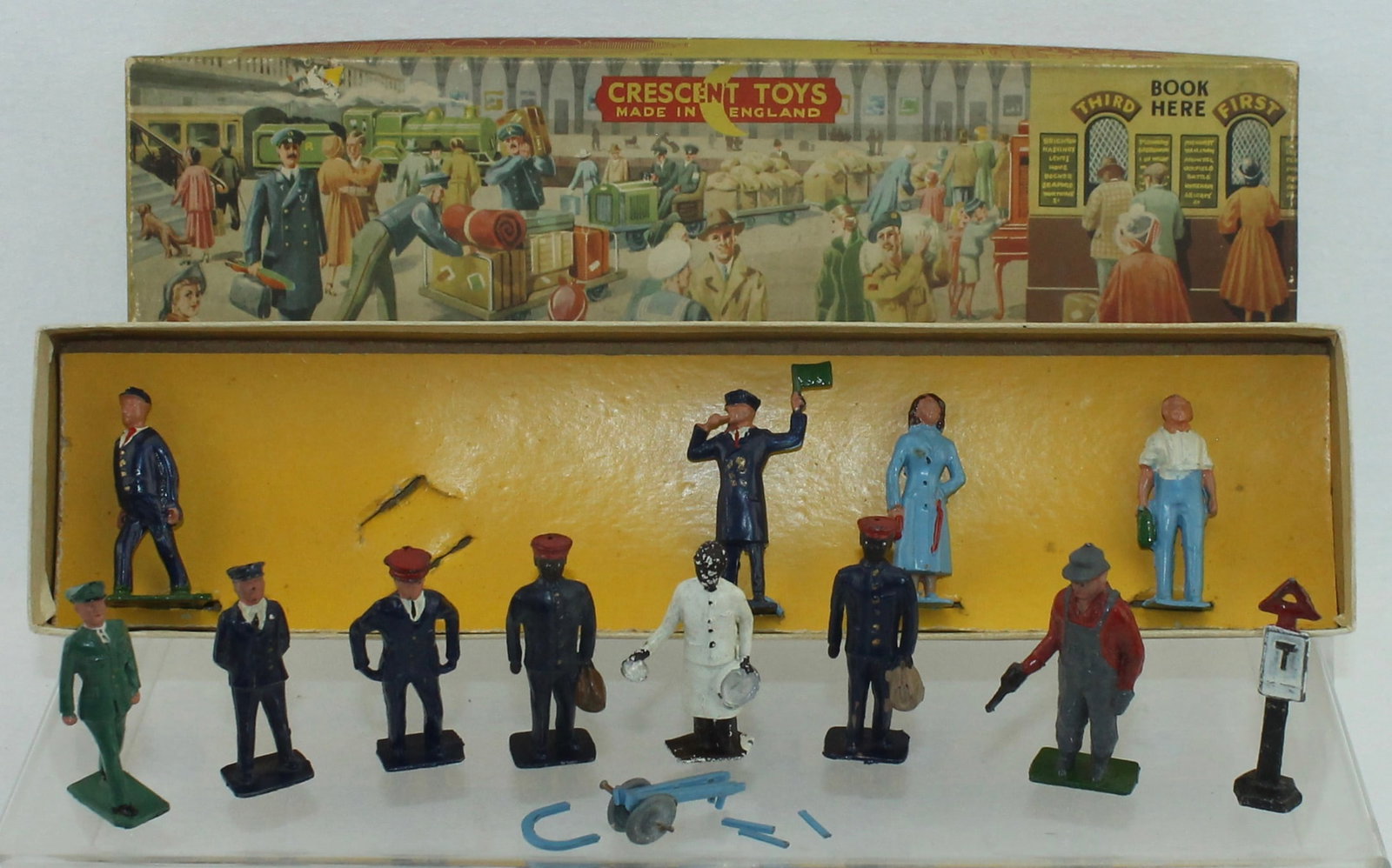 Crescent Lot Train Station Staff: Lot includes Small Box of Station Figures with Trolly and an Assortment of Loose Station Staff and Street Sign. 12 Pieces. Condition Good to Excellent. Trolly Distressed in Pieces. Box Good.