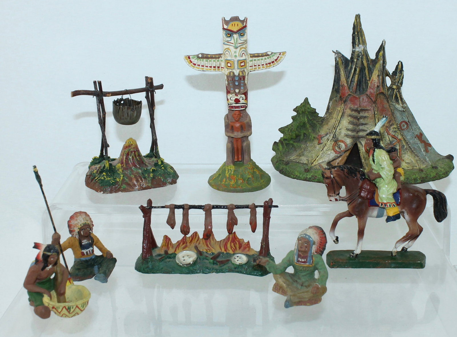 Elastolin Lot North American Indian Encampment: Composition. 7cm. Includes 3 Seated Indians, Mounted Squaw with Small Child, Seated Chief with Peace Pipe, Totem Pole, Teepee and 2 Cook Fires. 10 Pieces. Condition Good to Very Good. No Box.