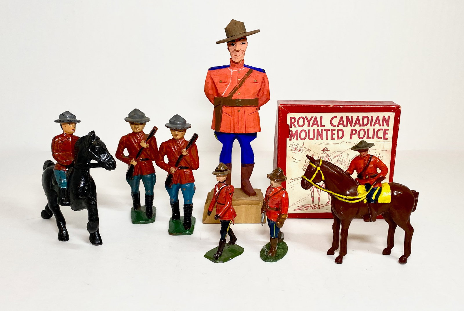 Assorted RCMP Figures: Large wooden carved figure, aluminum officer with pistol, Britains officer, three Grey Iron, and one Crescent Mounted figure. 7 total pieces. Near mint to excellent condition. One box in excellent con