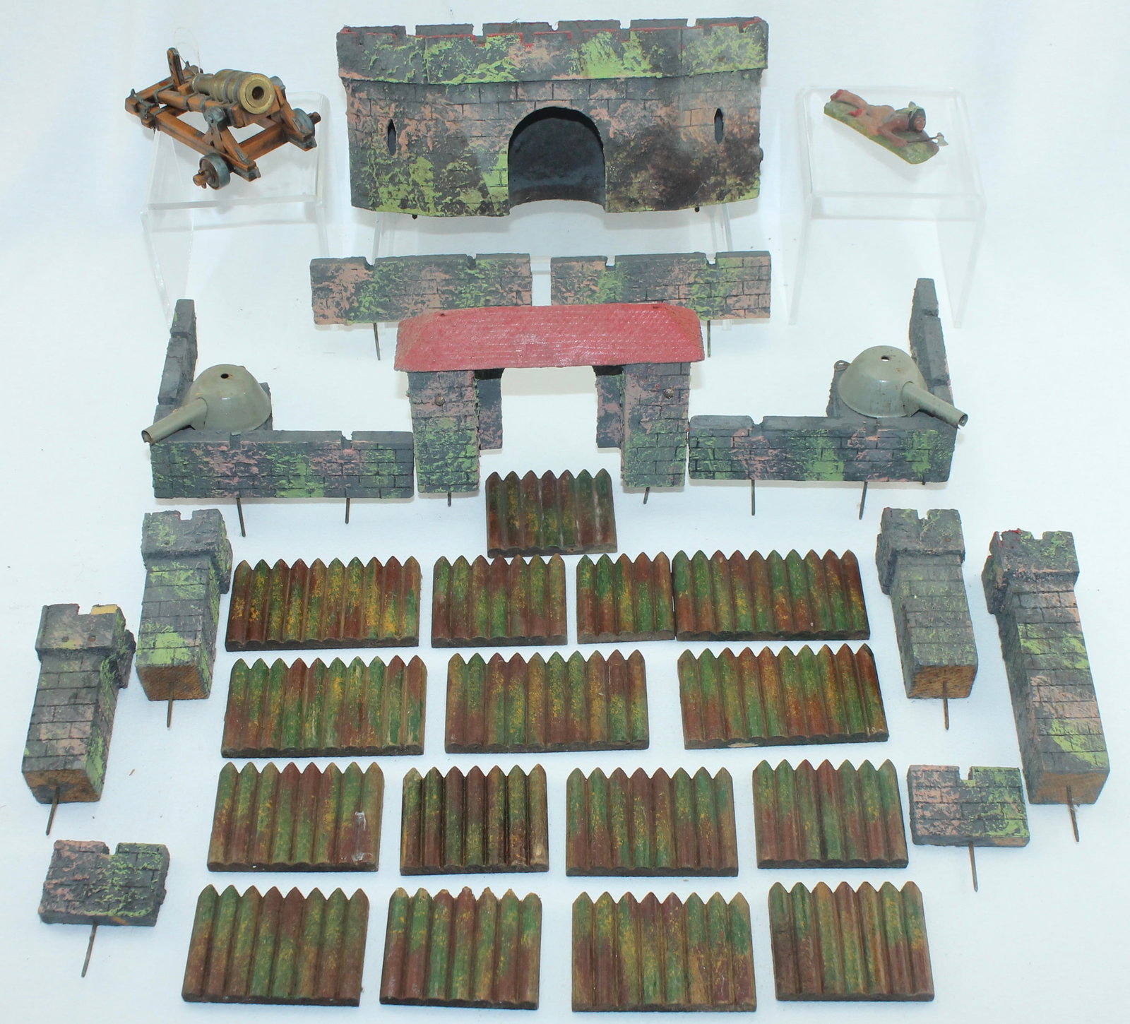 German Made Fortress and Stockade Elements: Lot includes Composition Fortress Walls, Turrets and Entry Gate by Unknown German Maker, Possibly Elastolin with 2 Detached Tin Plate Pea Shooting Cannons. Also includes 15 Stockade Fence Sections, El