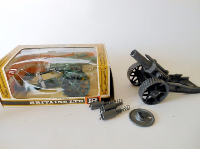 Britains Set #9704 Howitzers: Post War and Pre-War. 2 pieces. Post War example in original cellophane fronted box. Condition excellent. Box very good. Pre-War example in smoke grey version with a number of shell casings. 2 pieces.