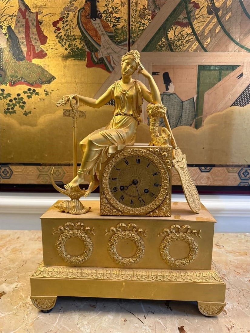 French Empire Gilt Bronze Figural Mantel Clock: Elegant French Empire mantel clock featuring a seated classical maiden in flowing drapery above a richly cast clock case. The figure is accompanied by nautical motifs including an anchor, shell, and