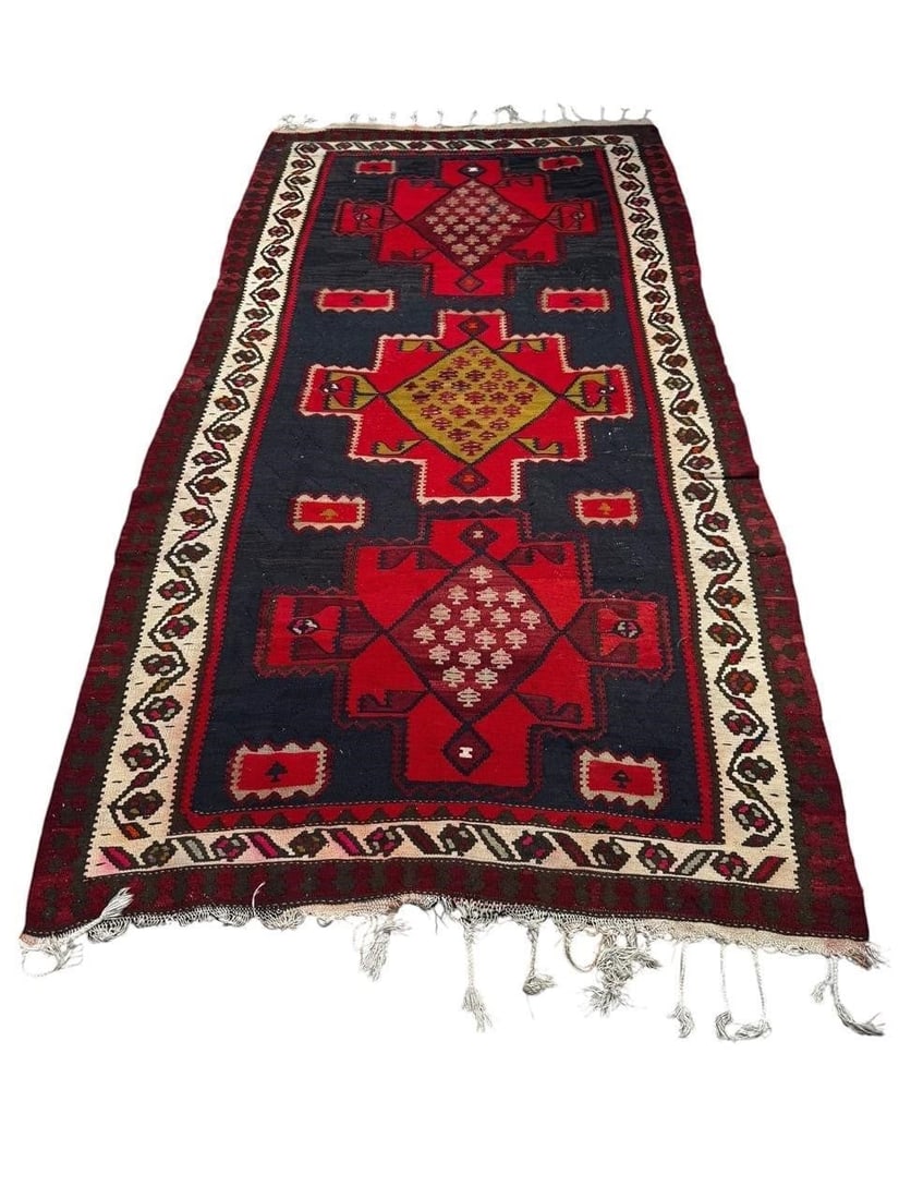 Early 20th c. Persian Kilim Rug: Early 20th century Persian handwoven kilim rug featuring bold geometric medallions set against a deep indigo field with ivory borders and vibrant red accents. Woven in flatweave construction with trad