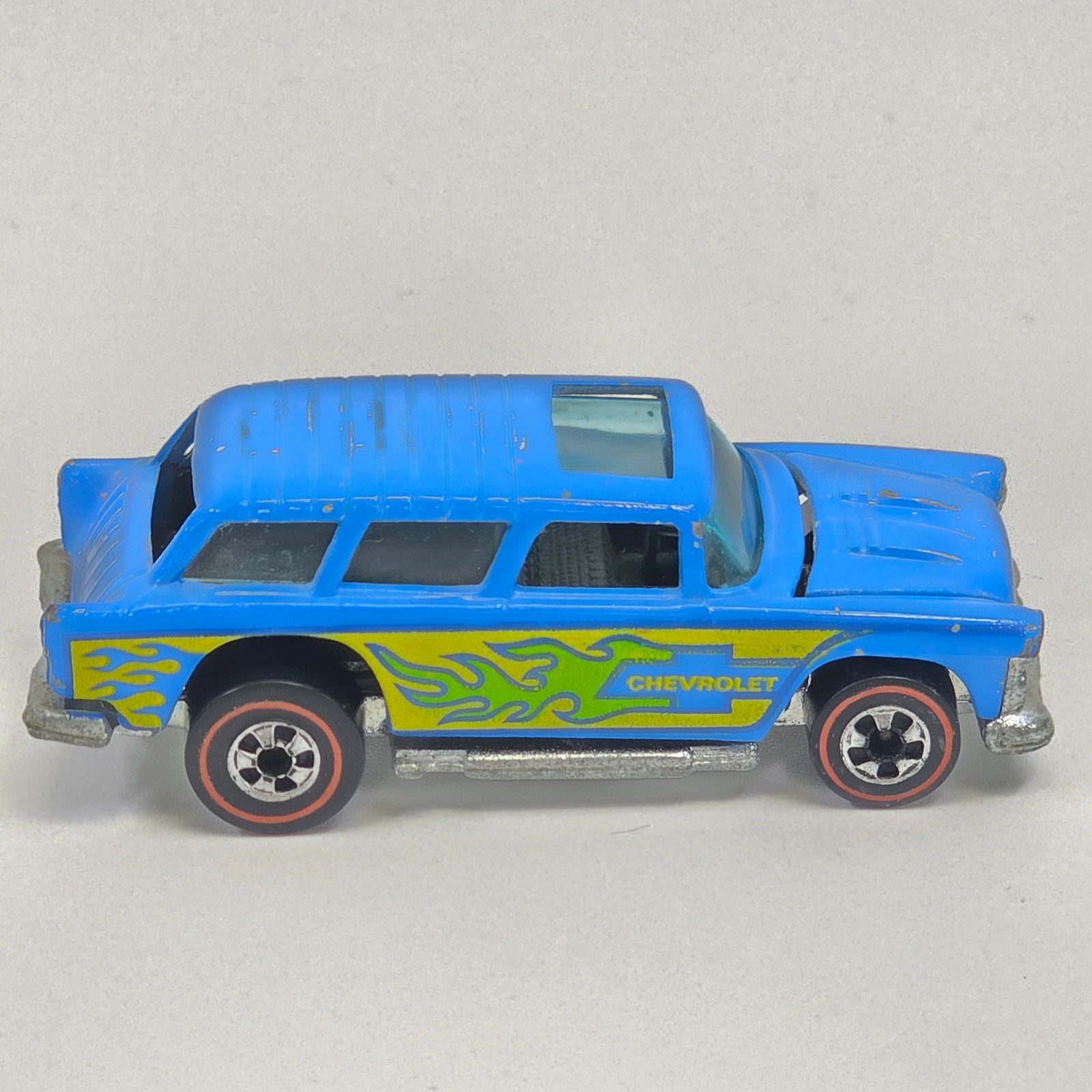 Hot Wheels Redline Alive '55: Flying Colors Alive '55 - Light Blue - Green and Yellow tampos - Dark Interior Good condition, has scattered chips and hard edge wear as seen. Glass is good. Wheel chrome is excellent. Base is clean.