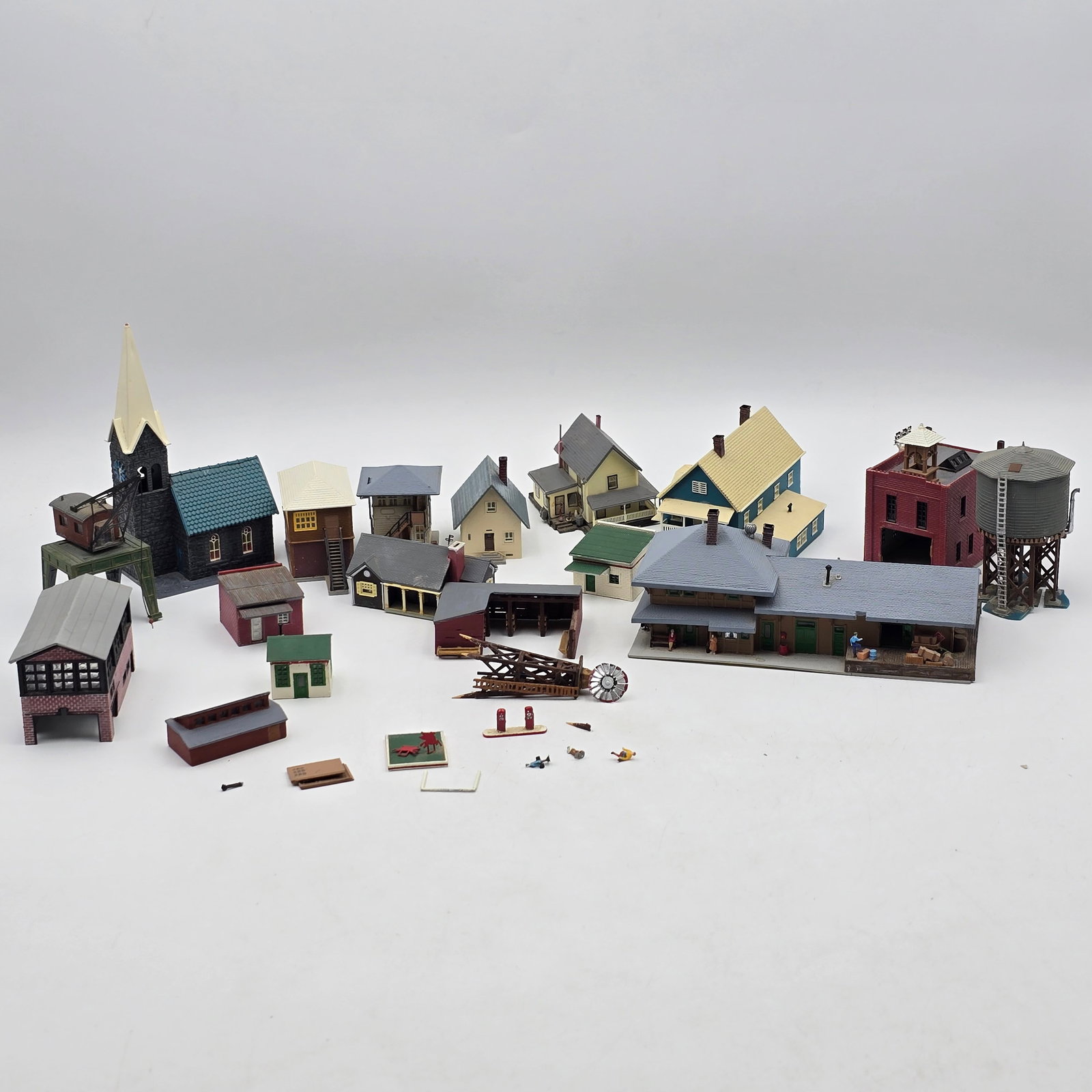 Lot of 23 Model Village Buildings: Lot of model buildings and accessories for train layouts or diorama scenes. Includes a variety of structures such as houses, storefronts, a church, water tower, and small accessory pieces. Items