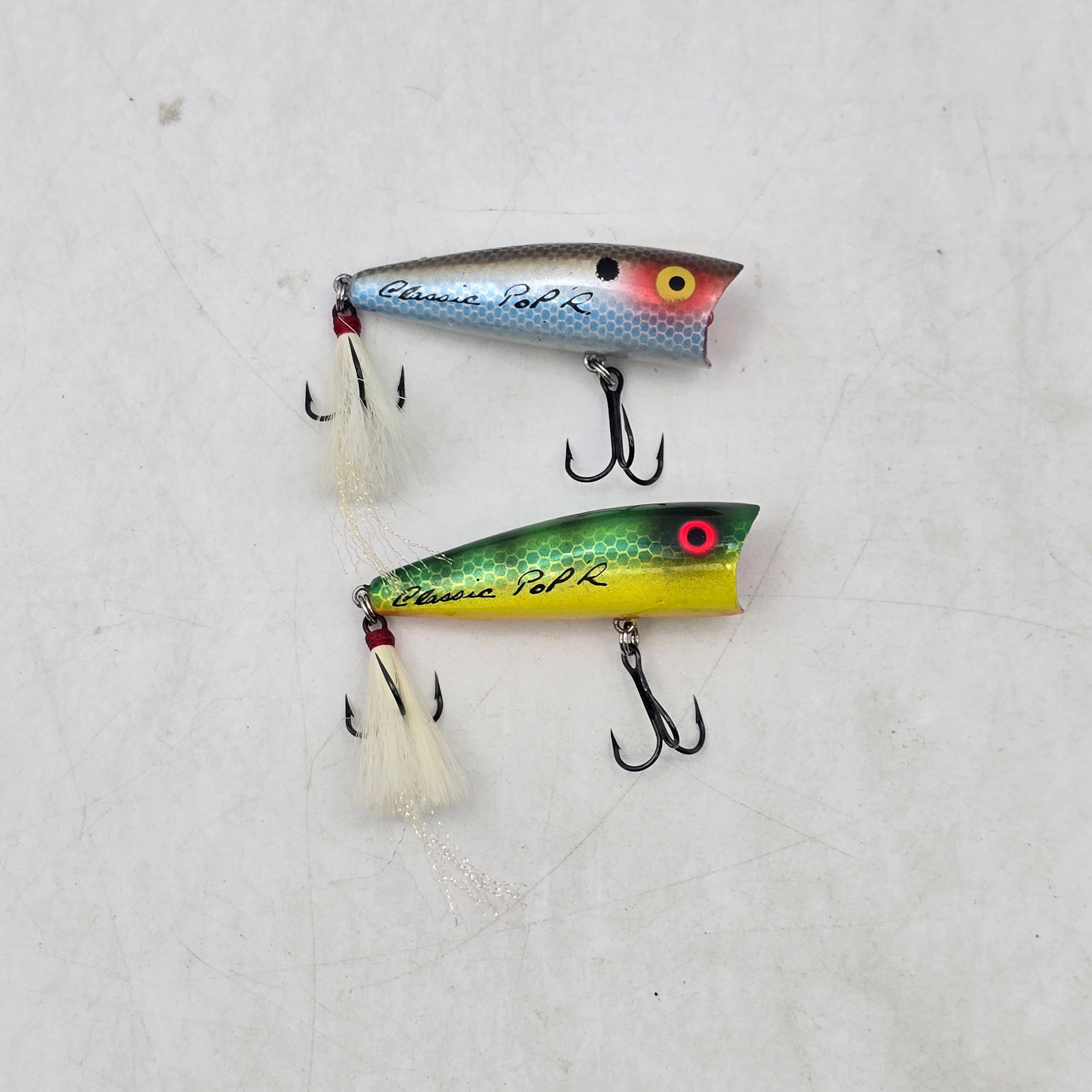 Creek Chub Lures 2pc: Lot of 2 Creek Chub Fishing Lures. Includes popper-style topwater lures in classic finishes with feathered treble hooks. Designed to create surface disturbance and attract strikes. Items show signs
