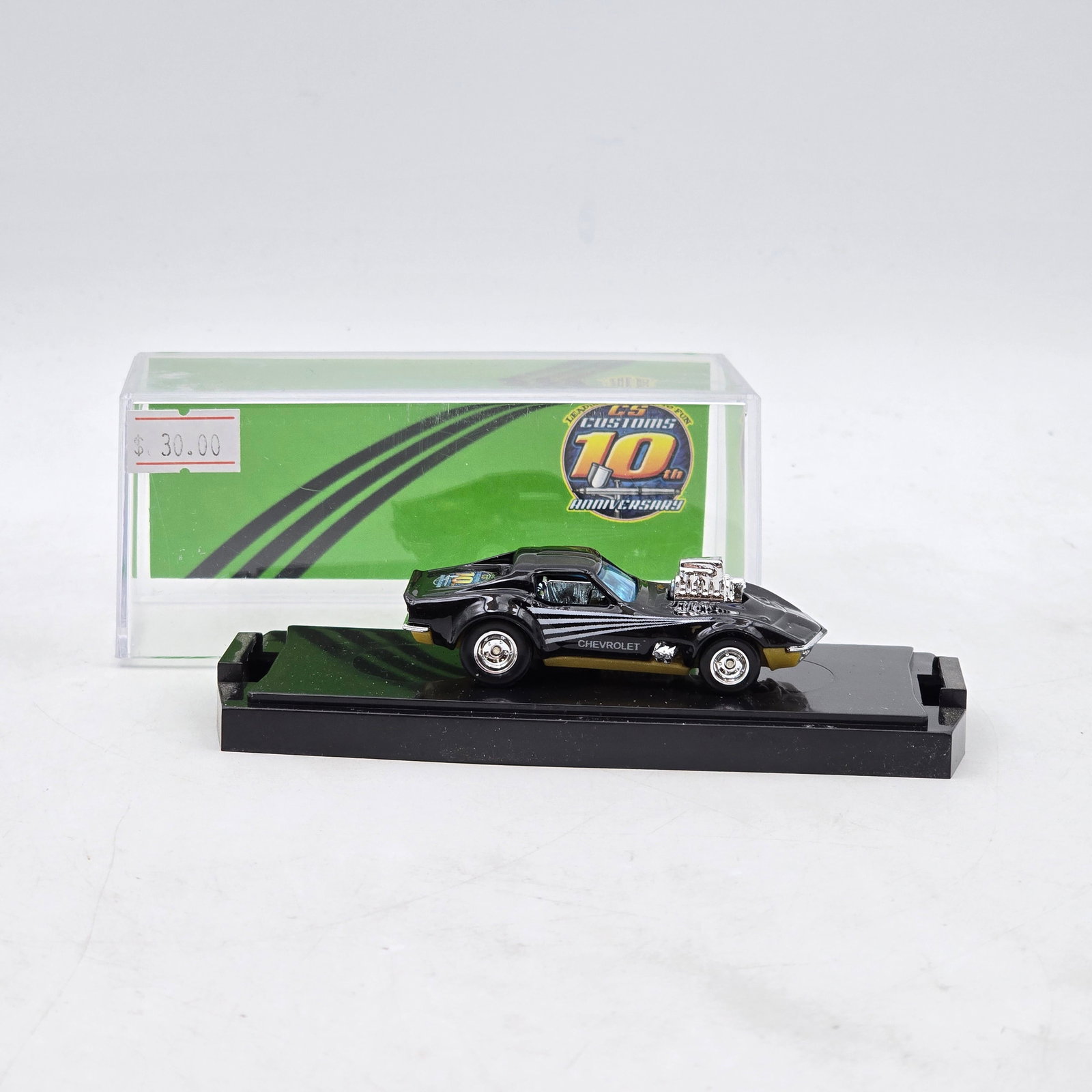 Chris Stangler Customs Chevrolet Custom: Hand-built custom Chevrolet diecast by Chris Stangler Customs featuring black paint, exposed chrome engine detail, anniversary graphics, and custom wheel setup. Display backdrop highlights the CS