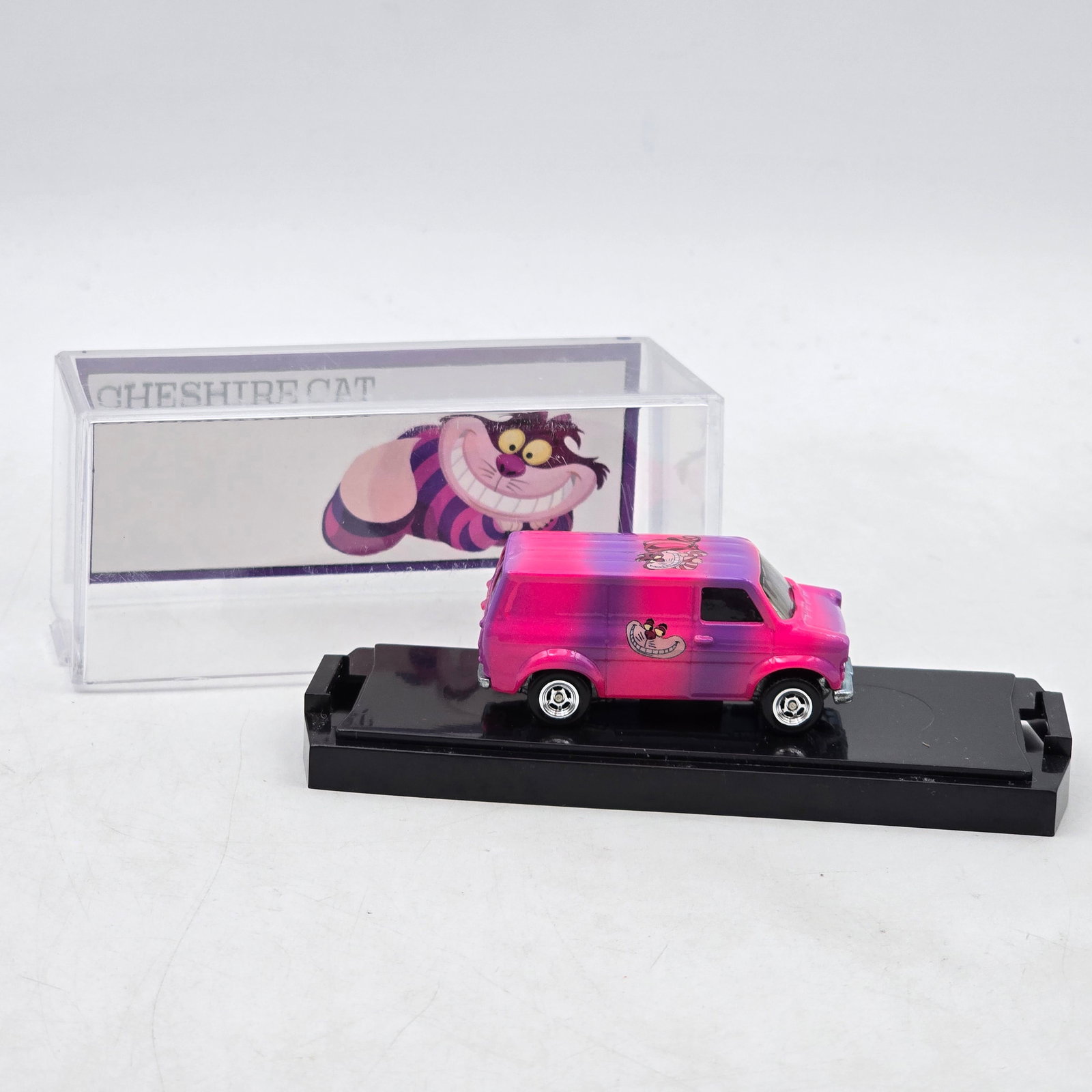 Chris Stangler Customs Cheshire Cat Van: Hand-built custom van by Chris Stangler Customs featuring bright pink-to-purple fade paint, Cheshire Cat graphics, and custom chrome wheel detail. Includes matching themed backdrop insert inspired by