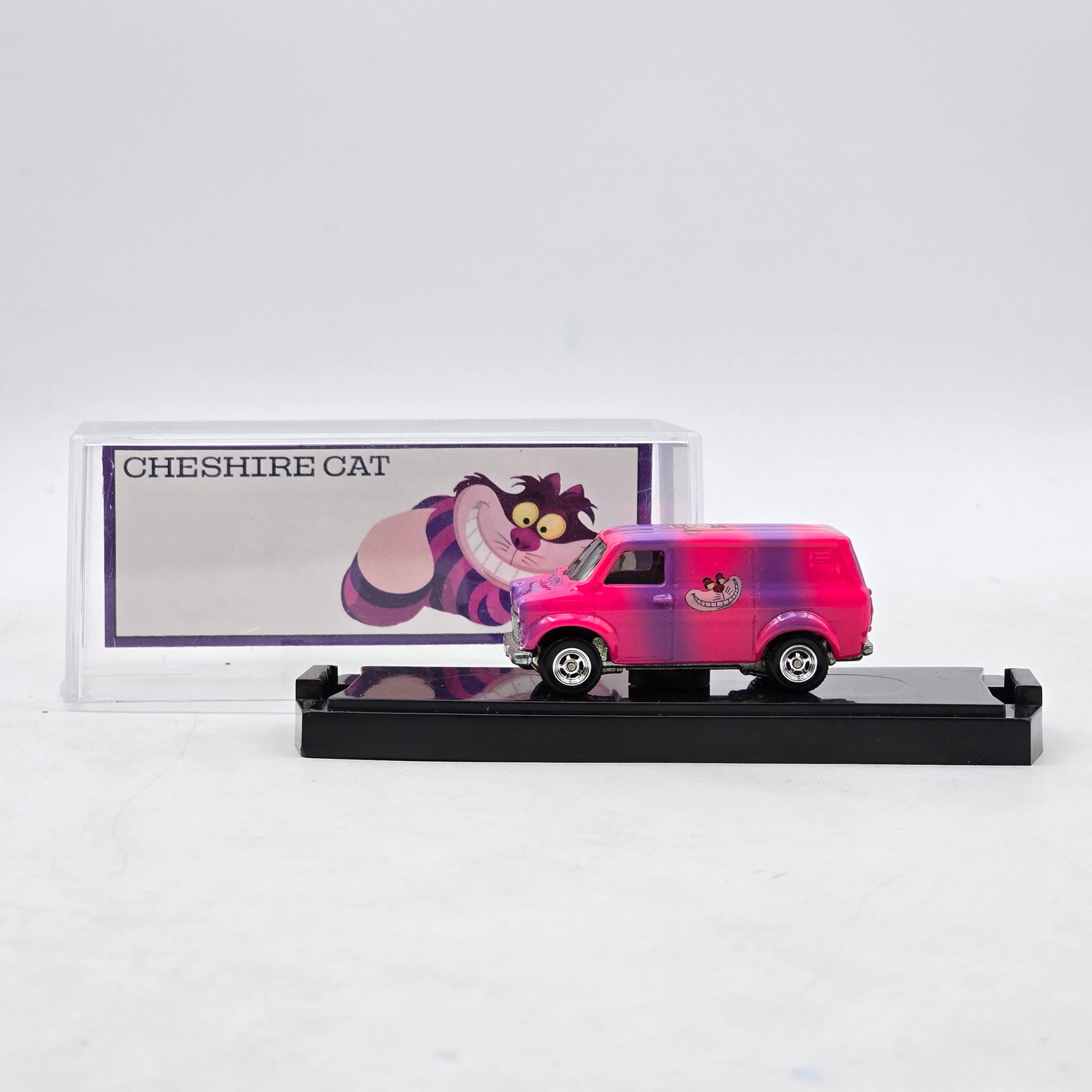Chris Stangler Customs Cheshire Cat Van: Hand-built custom van by Chris Stangler Customs featuring bright pink-to-purple fade paint, Cheshire Cat graphics, and custom chrome wheel detail. Includes matching themed backdrop insert inspired by 