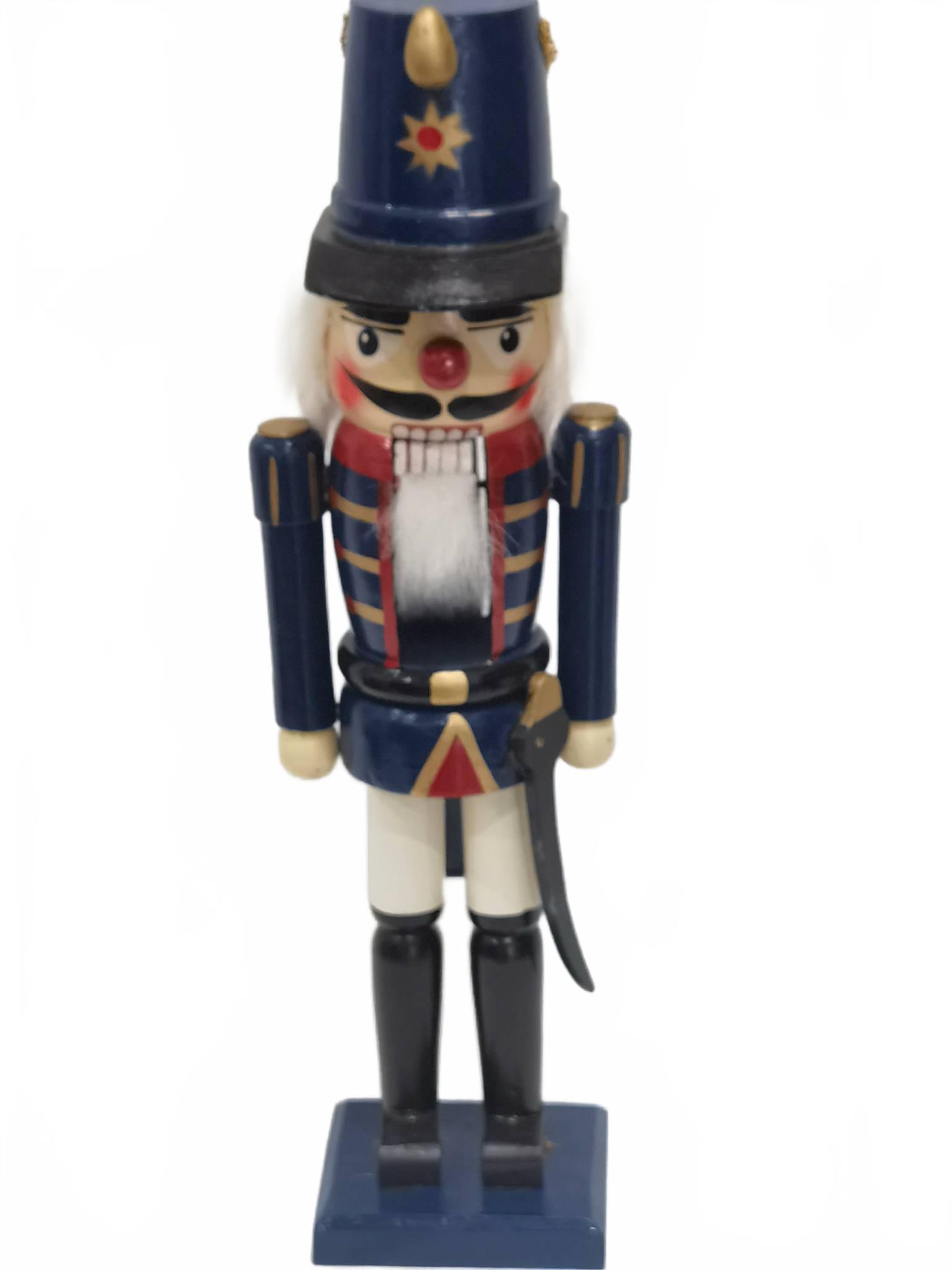 Wooden Soldier Nutcracker Blue Uniform Red Nose: Wooden nutcracker with blue uniform, white beard, sword, and tall hat featuring a red nose and gold details. 15in by 4.5in