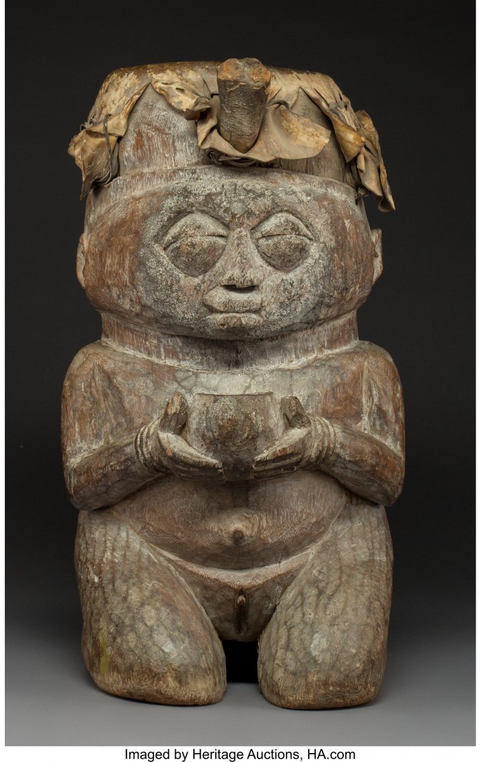A Yoruba Drum Nigeria For the Shango cult, car: A Yoruba Drum Nigeria For the Shango cult, carved as a plump kneeling female figure holding a bowl before her, a child at her back, the hide top secured with large wood pegs (two missing), traces of k