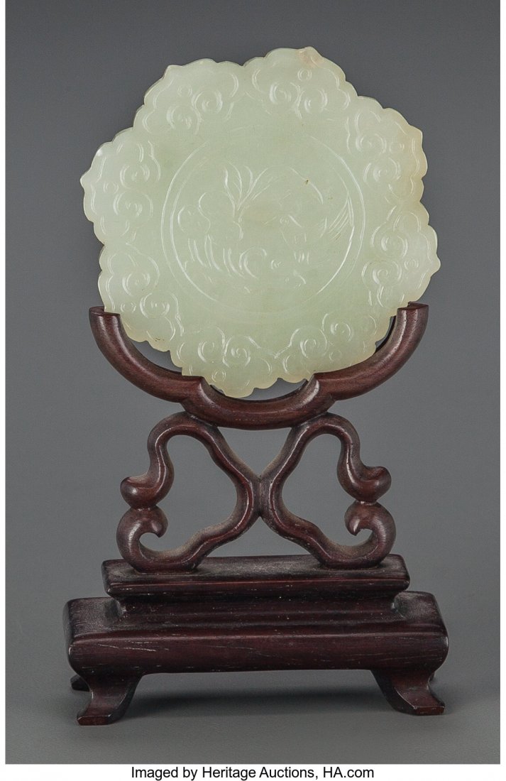 A Chinese Carved Pale Green Jade Bi Disk on Carv: A Chinese Carved Pale Green Jade Bi Disk on Carved Wood Stand 4-1/2 inches high (11.4 cm) The floriform disk with a central medallion to front depicting a bird within fruited foliage, bas relief flowe