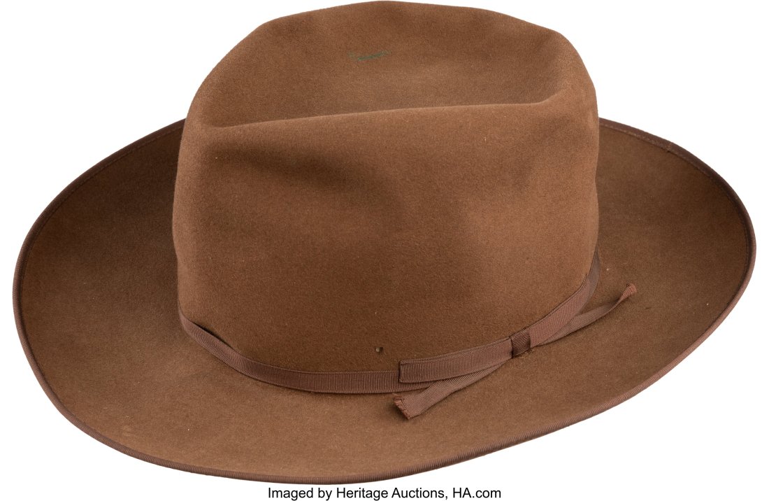 Director John Ford's Personal Fedora Owned by Jo: Director John Ford's Personal Fedora Owned by John Wayne (1950s). Vintage original mocha brown beaver felt fedora with thin grosgrain ribbon hatband. Stamped in gold gilt on th