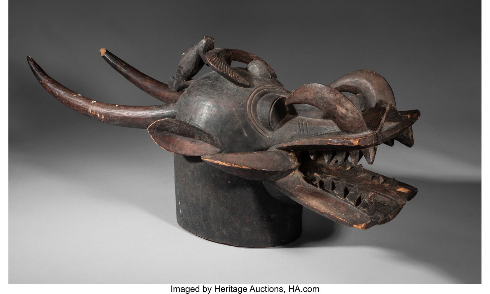 A Senufo Helmet Mask, kponyugo Ivory Coast, mid: A Senufo Helmet Mask, kponyugo Ivory Coast, mid to late 20th century Carved of blackened wood in a typical zoomorphic form: a large cow head with a human nose, crocodile mouth