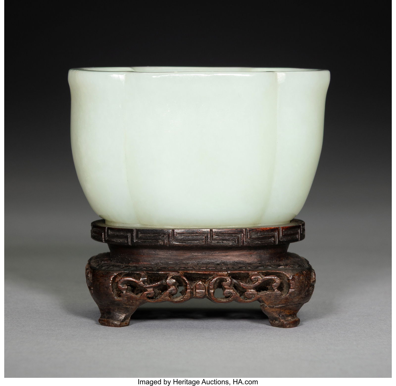 A Carved Celadon Jade Quatrefoil Cup on Carved W: A Carved Celadon Jade Quatrefoil Cup on Carved Wood Stand 1-5/8 x 2-3/4 x 2 inches (4.1 x 7.0 x 5.1 cm) (work) HID03101062020 © 2026 Heritage Auct