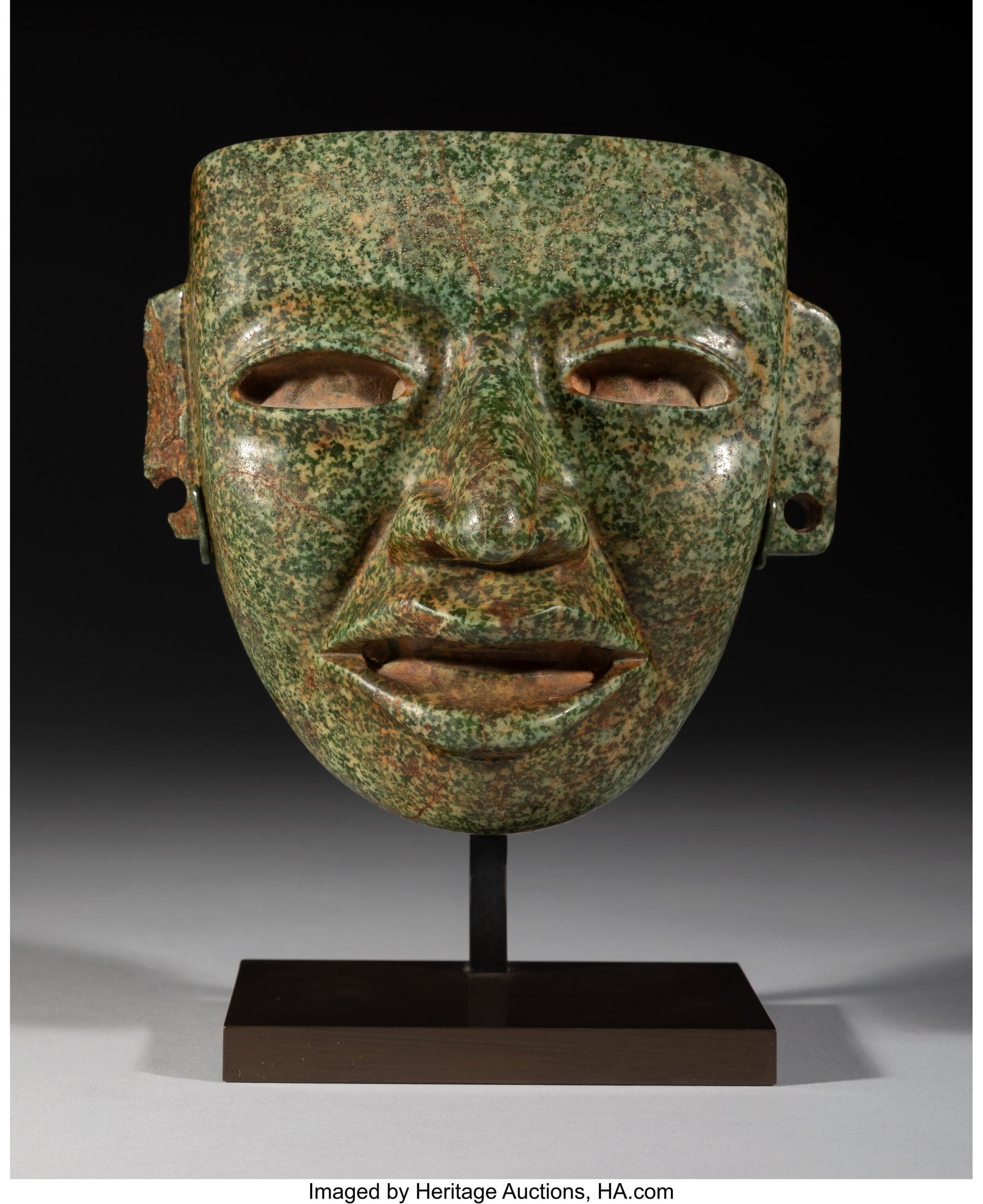 A Teotihuacan Mask Mexico, c. 250–600 AD Car: A Teotihuacan Mask Mexico, c. 250–600 AD Carved from green hardstone with evenly distributed speckling in darker and lighter green, the mask presents a youthful visage with a 