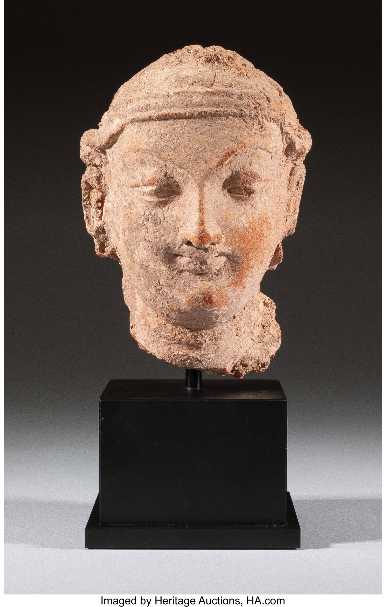 An Indian Carved Sandstone Head of a Figure on S: An Indian Carved Sandstone Head of a Figure on Stand 6-1/2 x 4-1/4 x 4-1/2 inches (16.5 x 10.8 x 11.4 cm) (work) 9-1/2 x 4-1/4 x 4-1/2 