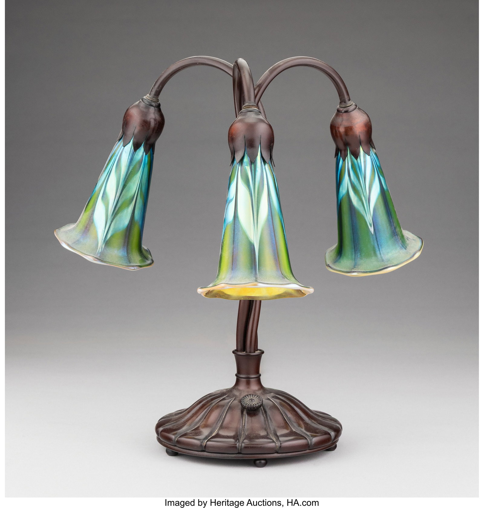 A Buffalo Metal Works Patinated Bronze Three-Lig: A Buffalo Metal Works Patinated Bronze Three-Light Table Lamp with Orient & Flume Iridescent Glass Shades, circa 1980 Marks to shades: Orient & Flume, LS 1977g242 Marks to ba