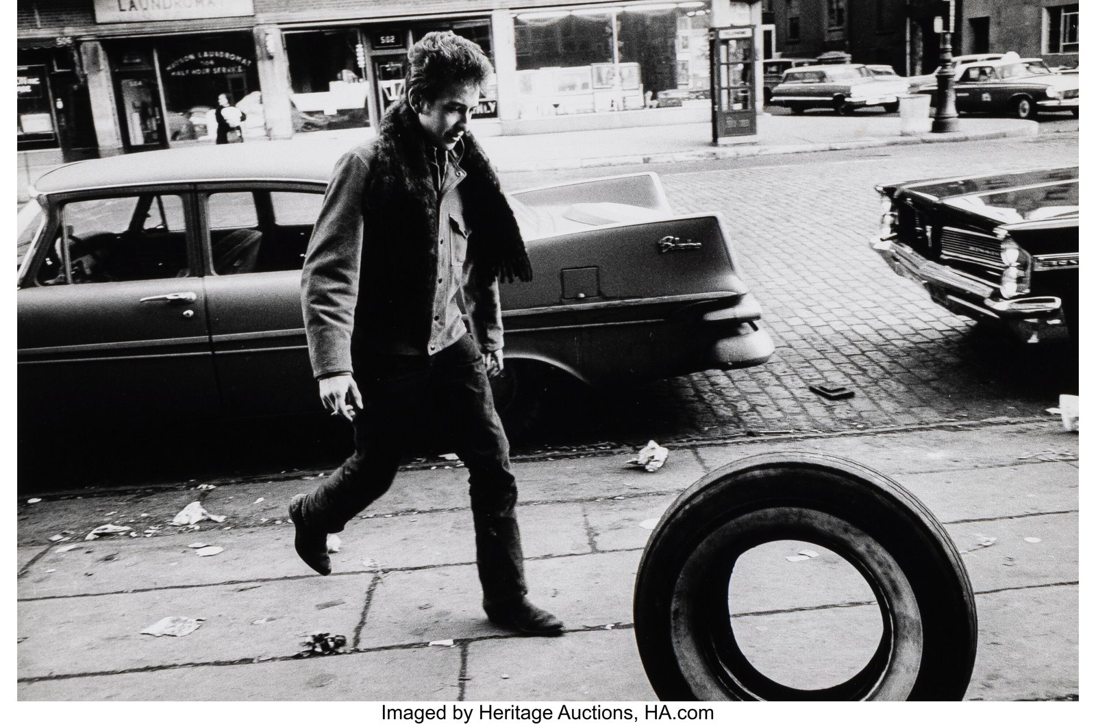 Jim Marshall (American, 1936-2010) Bob Dylan Kic: Jim Marshall (American, 1936-2010) Bob Dylan Kicking Tire, Seventh Avenue, New York City, 1963 Gelatin silver print, printed 1980 6-1/4 x 9-3/4 inches &