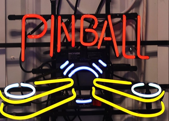 PINBALL NEON: •Design: The sign has two distinct sections. The top section spells out the word "PINBALL" in a bold, red neon script. The bottom section is a stylized representation of the pinball machine's pl