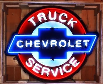 CHEVROLET TRUCK SERVICE NEON 42 x 33 x 6: NEW reproduction -A vibrant, lit-up neon sign. It's circular in shape with a prominent red outer ring. Inside, there's a blue Chevrolet bowtie logo. The words "TRUCK" are at the top in white neon,