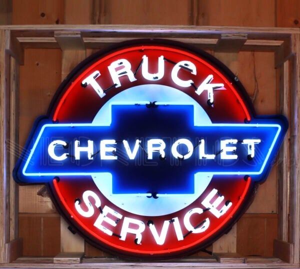 CHEVROLET TRUCK SERVICE NEON 42 x 33 x 6: NEW reproduction -A vibrant, lit-up neon sign. It's circular in shape with a prominent red outer ring. Inside, there's a blue Chevrolet bowtie logo. The words "TRUCK" are at the top in white neon,