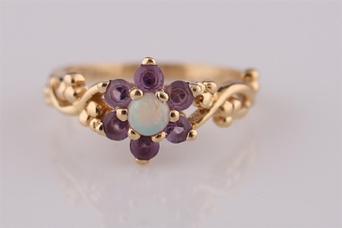14kt Yellow Gold, Opal, and Amethyst Ring: 14kt yellow gold ring with central white opal surrounded by six amethyst gemstones. Floral design band. Interior of band marked "14K". Size: 6. Weight: 2.5 g.