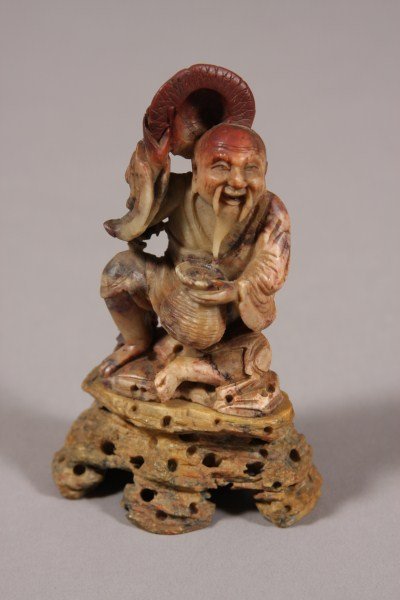 Two Chinese Carved Soapstone Figures, Chinese, 20t: Chinese, 20th century. A seated man holding a basket and a censor flanked by foo dogs. Former H: 5" Condition: The censor has been broken and glued.