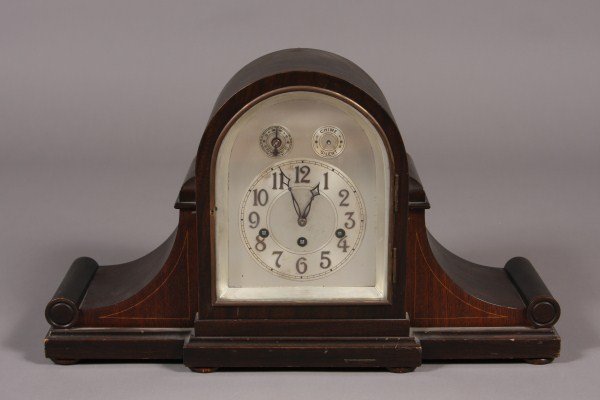 Unghans Mahogany Finished Mantle Clock, German, 20: 20th century. Domed case enclosing an Arabic numeral dial. Dimensions: H: 12 1/2" L: 22" Condition: Edges are nicked. Finish is worn. Finish is worn on the metal and dial is worn.