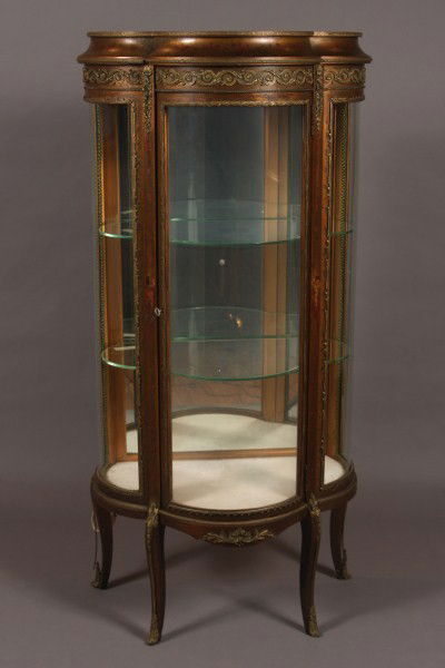 Louis XV Style Gilt & Brass Mounted Vitrine, French,: 20th century. Shaped demi-lune case decorated with trailing vines and putti. Condition: Gilt finish overall is darkened. Bronze mounts are pulling off the back legs. Molded brass edges are pulling up