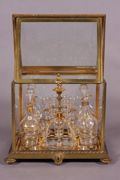 Gilt Brass and Glass Tantalus: Gilt Brass and Glass Tantalus. Continental, late 19th, early 20th Century. WIth glazed case enclosing Four (4) decanters and 16 cordial glasses. H: 1 1/2", W: 12", D: 9"Condition: One decanter appears