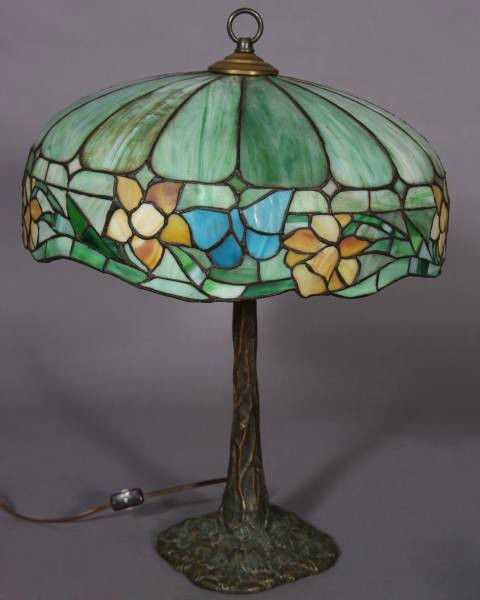 Arts and Crafts Bronze and Leaded Glass Table Lamp: Arts and crafts bronze and leaded glass table lamp. American, early 20th century. Domed shade with floral and butterfly border. the bronze base moulded as a tree trunk and leaves. Height 22", diameter