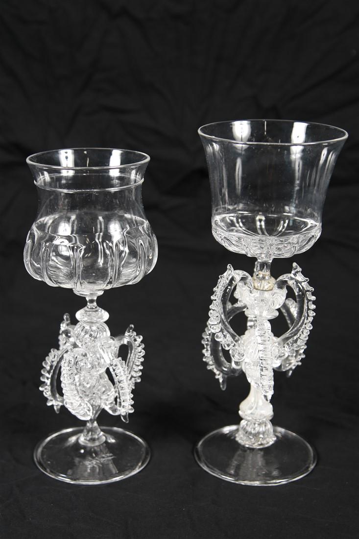 Pair of Clear Art Glass Tipetto Goblets: Glass. Larger: Height: 9 5/8", Diameter: 3 7/8". Smaller: Height: 9", Diameter: 3 1/2". Glass goblets with detailed filigree details at the stem. Signatures to undersides.