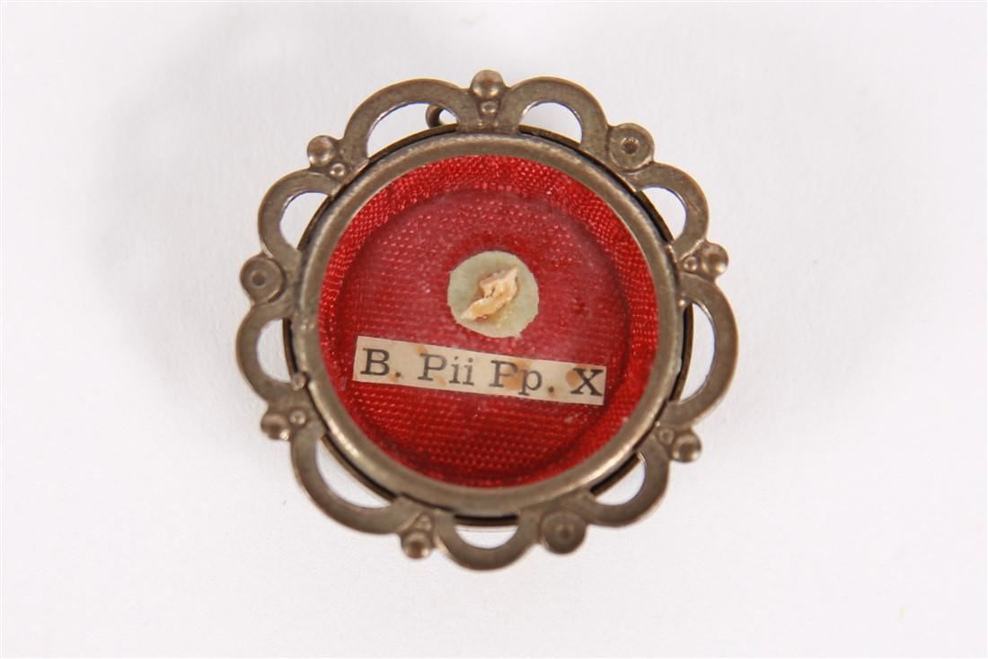 Pope Pius X (B. Pii Pp. X) Round Metal Reliquary: Metal, glass, silk. Diamater: 1 7/8". Scalloped edge silver colored pendant with red silk lining behind relic and label which reads, "B. Pii Pp. X". Provenance: Comes with certificate of authenticity