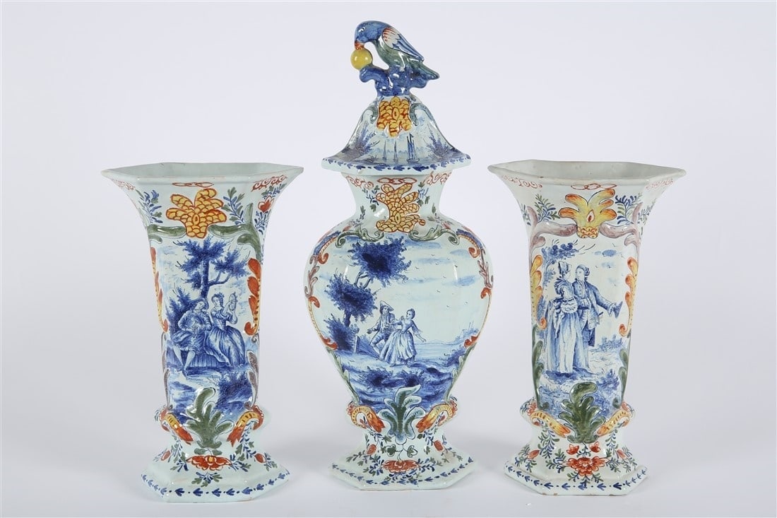 Dutch Polychrome Delftware Garniture Set: Polychrome painted delftware. Lidded vase: Height: 15", Length: 6 1/4", Depth: 4". Side vases: Height: 10 1/2", Length: 6 1/2", Depth: 4 1/2". Dutch polychrome painted delftware garniture set consisti