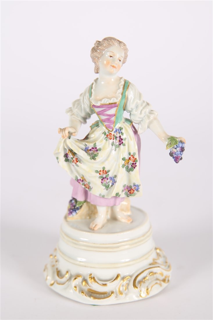 Meissen, Porcelain Woman with Grapes Figurine: Meissen (German, established 1710). Porcelain. Height: 6", Diameter: 3". Woman in a floral dress holding a bunch of grapes. Crossed sword logo, 28 painted to underside.