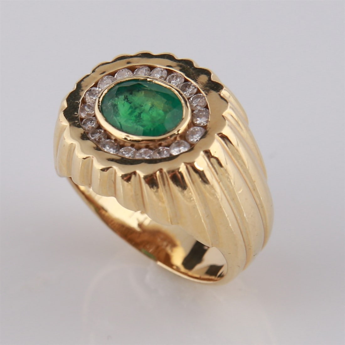 14k Yellow Gold, Emerald, and Diamond Ring: 14k yellow gold ring with emerald and diamonds. One oval-cut center emerald surrounded by eighteen (18) small diamonds. Marked "14K' to the interior of the band. Size: 7. Total weight: 8.6g.