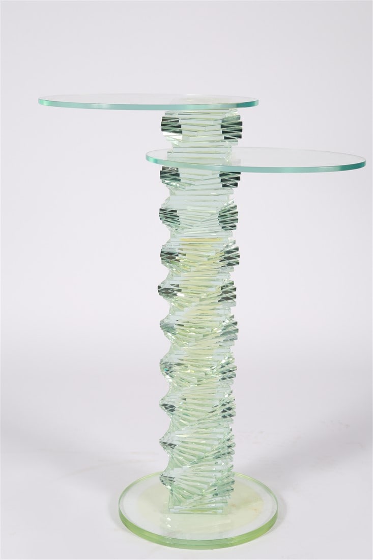 In the Style of Ravello, Glass Prism Side Table: Glass. Height: 39 3/8", Length: 29", Depth: 15". Glass prism table comprised of stacks of glass forming the base of the table and two oval-shaped glass panels forming the tabletops. Appears unsigned. 