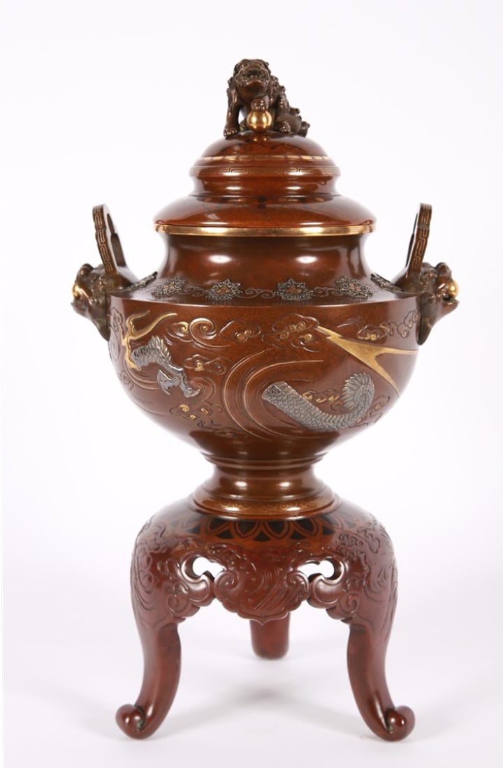 Bronze and Mixed-Metal Japanese Koro: Bronze, mixed metal. Height: 21", Diameter: 12". Bronze and mixed-metal Japanese koro. Tripod base. A silver dragon to the body of the piece. Shishi head handles and finial.