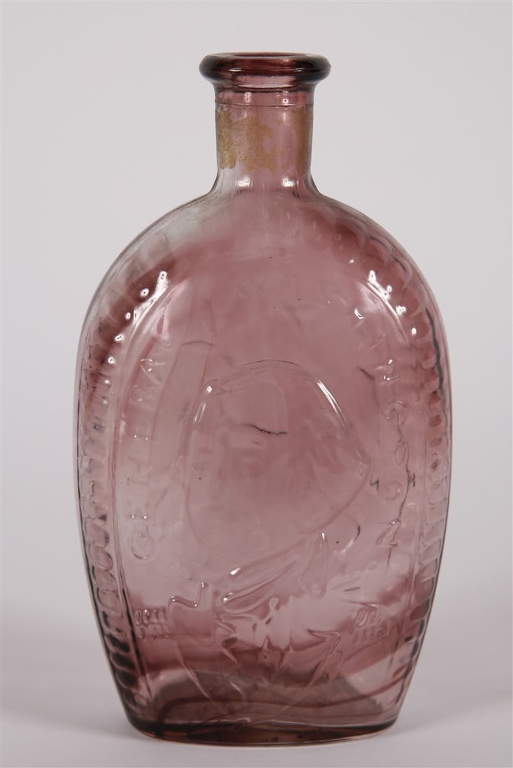 General Washington Glass Flask: Glass. Height: 8 3/4", Length: 4 3/4", Depth: 2 1/4". Violet or purple hued glass flask. One side with a portrait of George Washington that reads, "General Washington", and the other side with the Uni