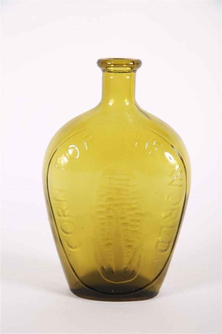 "Corn for the World" Glass Flask: Glass. Height: 8 1/2", Length: 5 1/4", Depth: 2 1/2". Yellow-green tinted glass flask. On one side the flask shows an image of an ear of corn and reads, "Corn for the World". Reverse side is blank.
