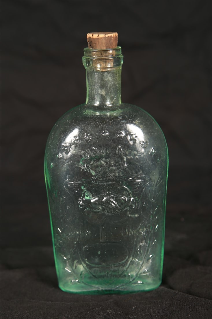 Civil War Union Glass Flask: Glass. Height: 6 1/2", Length: 3 1/4", Depth: 1 1/2". Clear glass flask. One side reads, "Union" with an image of two hands clasped surrounded by laurels and stars. The other side with the United Stat