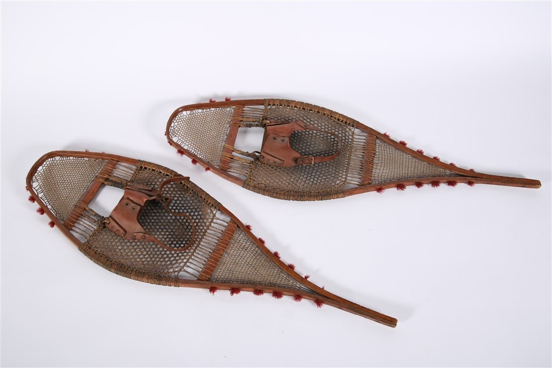 Pair of Wood and Leather Snow Shoes: Wood, leather. Length: 43 1/2", Width: 13 1/4". Pair of wood and leather snow shoes. Wood frame with woven leather and red binding. Leather straps.