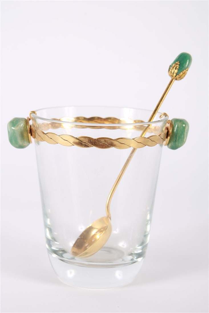 Glass and Brass Ice Bucket with Matching Spoon: Glass, brass, stones. Bucket: Height: 6 1/2", Diameter: 5". Spoon: Length: 9". Glass ice bucket with brass and green stone decoration. Matching brass spoon.