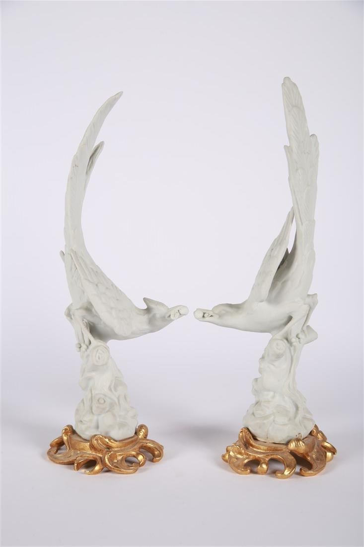 Pair of Bisque Porcelain Bird Figures: Bisque porcelain, gilt metal. Height: 13", Length: 4", Depth: 4". Pair of bisque porcelain figures depicting birds with twigs and a fruit in their beaks. Mounted on gilt metal scrolled bases.