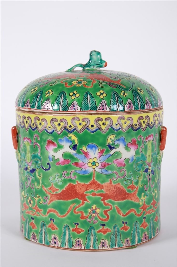 Green Chinese Porcelain Covered Storage Jar: Porcelain. Height: 9 1/2", Diameter: 6 3/4". Chinese porcelain covered storage jar. Green ground with yellow, red, and other colors. Lid with finial depicting an animal. Fish motifs. Unsigned.