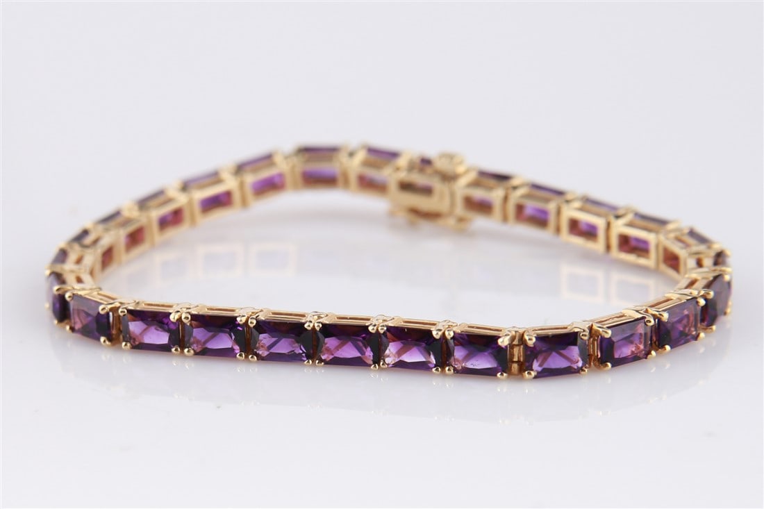 14k Yellow Gold and Amethyst Tennis Bracelet: 14k yellow gold and amethyst tennis bracelet. Includes twenty-seven (27) emerald-cut amethyst stones. Marked to the clasp "14K". Length: 7". Total weight: 15.7g.