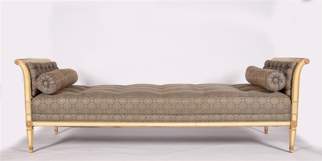 French Louis XVI Style Daybed: Wood, fabric. Height: 28 1/2", Length: 87 1/2", Depth: 28 1/4". Louis XVI style daybed with cream paint and gilt trim. Upholstered in blue and gold fabric with two matching bolster pillows.