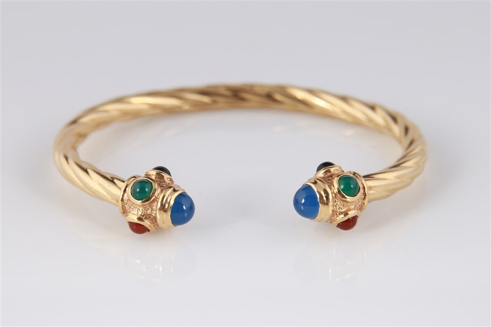 14k Yellow Gold Gem Stone Twist Bracelet: 14k yellow gold open bangle style bracelet with colored gem stones. Twisted cuff style with a crown of gem stones set on each end. Stamped "BA". The bracelet is set with: 2 round cabochon cut blue ony